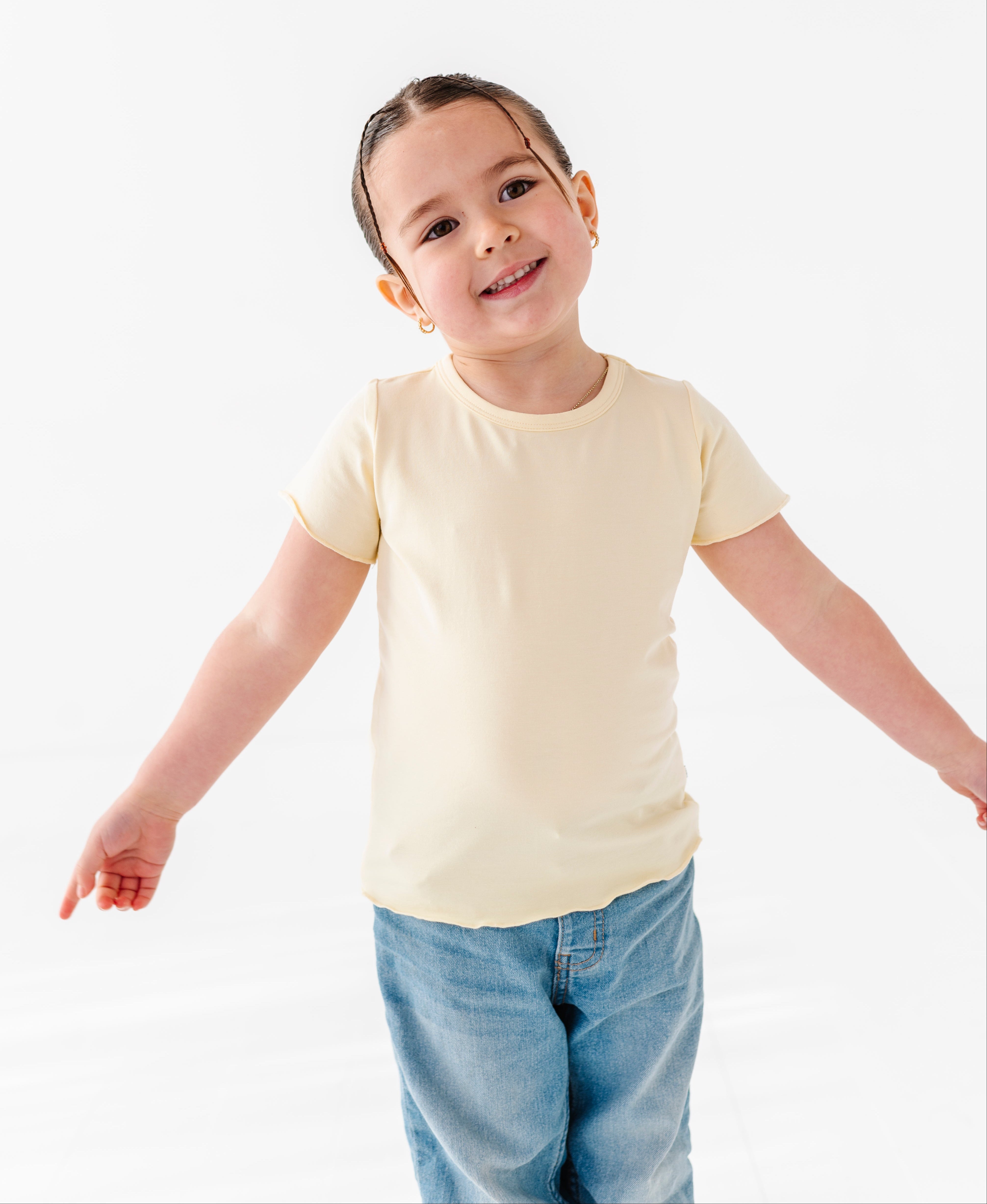 Child wearing a plain yellow t-shirt and blue jeans on a white background